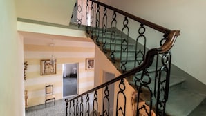 A staircase with ornate black metal railings and wooden handrails, leading to a room with striped walls and a chandelier.