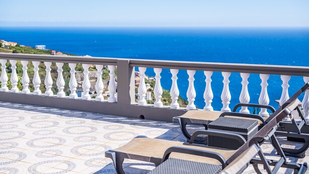 Un balcon avec vue sur la mer, des balustrades blanches et deux fauteuils de relaxation.