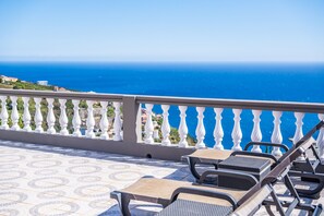 Un balcon avec vue sur la mer, des balustrades blanches et deux fauteuils de relaxation.
