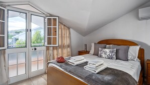Une chambre à coucher avec un lit, une table de chevet, une fenêtre avec des rideaux et une vue sur l’extérieur.
