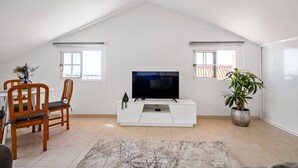 Une pièce avec un plafond blanc, un téléviseur à écran plat posé sur un meuble de télévision blanc, des chaises en bois, une table à manger et une plante en pot.