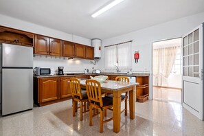 Une cuisine avec des meubles en bois, un réfrigérateur, un four à micro-ondes, une table avec des chaises et une fenêtre avec des rideaux.