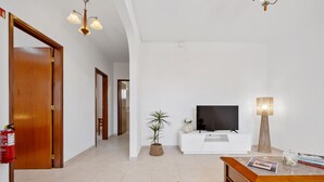 Una sala moderna con una mesa de centro de madera, mueble blanco para televisión, televisor de pantalla plana, planta en maceta y extintor.