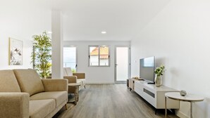 A modern living room with a sofa, a small table, a TV, and a plant.
