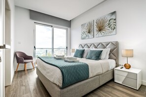A modern bedroom with a large bed, a nightstand, a chair, and artwork on the wall. - Villa Vellure by Madeira Sun Travel (Funchal)