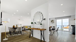 A modern living space with a dining area, a large decorative mirror, and a view of the sea.
