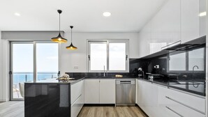 A modern kitchen with a black island, white cabinets, and a view of the sea through large windows.