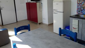 Una cucina compatta con tavolo, sedie, frigorifero, televisione e lavandino.