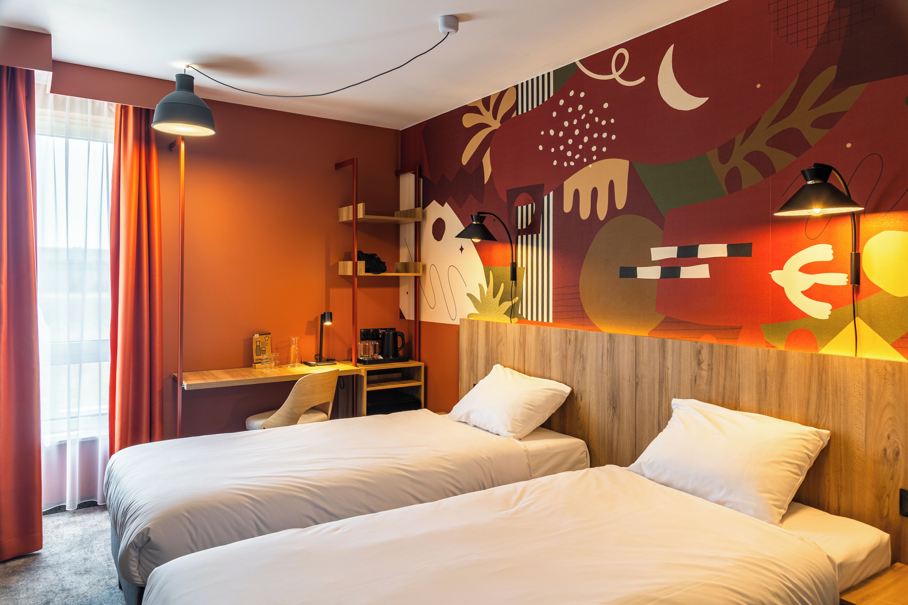 Habitación de hotel con dos camas, un escritorio y una pared decorada con arte abstracto.