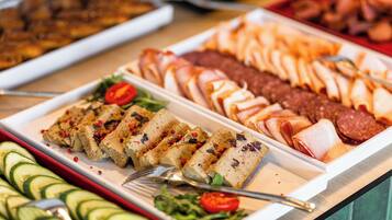 Un bufé con diversos alimentos, incluyendo carnes cortadas, verduras y un plato con guarnición roja.