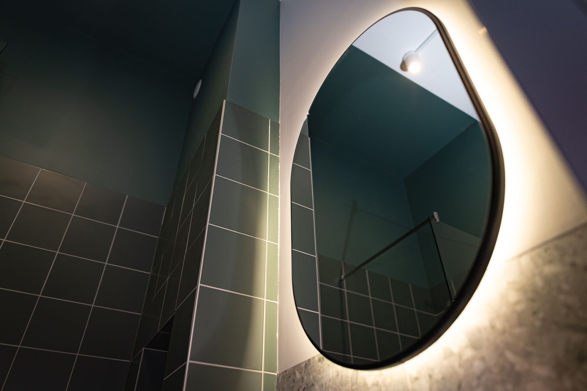 A bathroom with a large mirror, tiled walls, and a visible handrail.