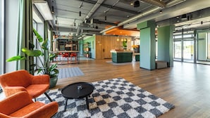 Un hall d’entrée spacieux, avec un tapis à carreaux, des fauteuils orange et une plante en pot.