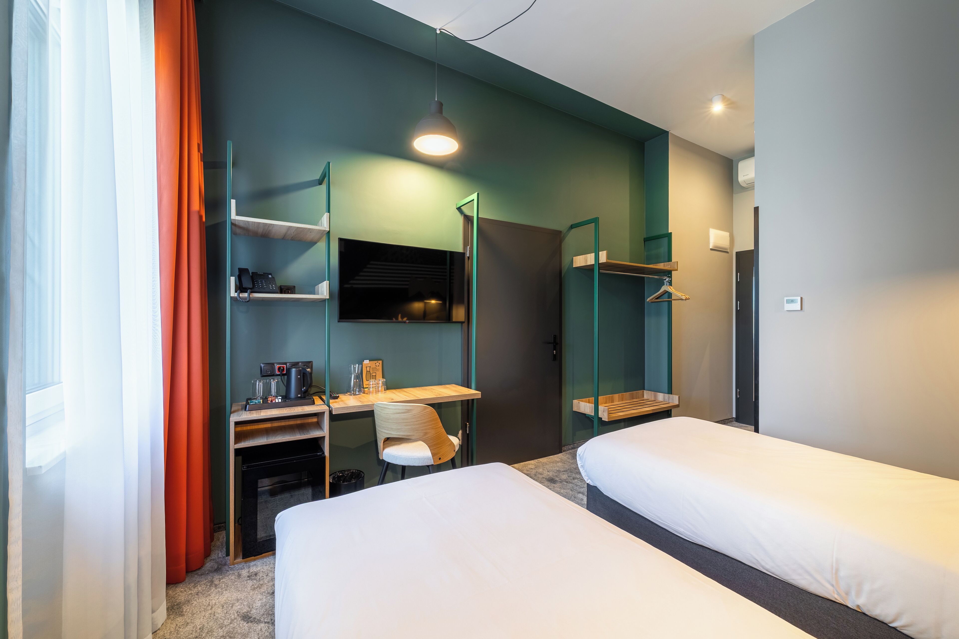 A hotel room with two beds, a desk with a chair, a mirror, and a wardrobe.