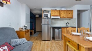 Een knus woongedeelte met kitchenette, een bank, een eettafel en een klein keukenhoekje met houten kasten en moderne apparatuur.
