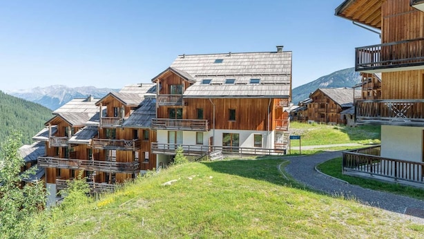 Een groepje houten chalets met balkons, gelegen tegen een bergachtige achtergrond.