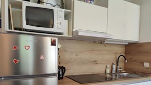 Een kleine keuken met een roestvrijstalen koelkast, een magnetron, een inbouwoven, een spoelbak en een vaatwasser.