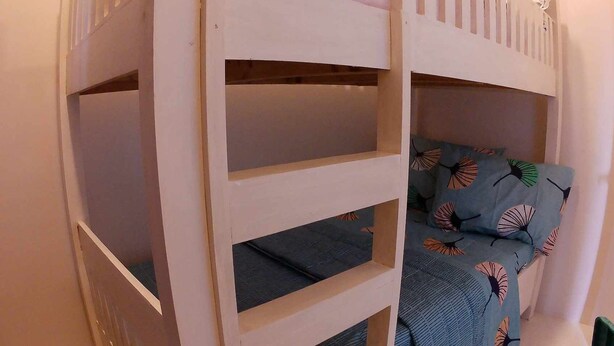 A bunk bed with a blue mattress and patterned pillows, against a plain wall.