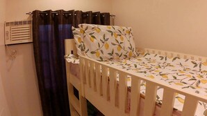 A small, single-bed room with a white bedspread featuring a lemon pattern, a dark curtain, and a wall-mounted heater.