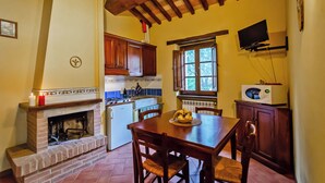 A kitchen with a fireplace, wooden cabinets, a dining table with chairs, a microwave, and a window with a view of trees.