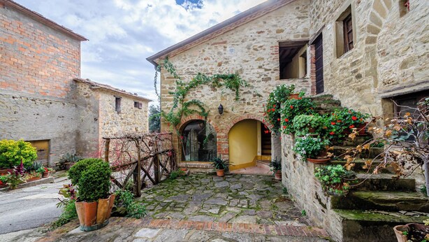 A stone building with a central archway, potted plants, and a cobblestone courtyard.