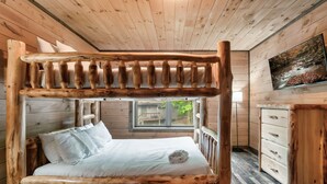 Ein rustikales Holzhäuschen mit einem Bett, das einen Holzrahmen hat, und Blick auf einen Wald durch ein Fenster.