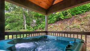 Ein Whirlpool mit einer Holzterrasse und Blick auf einen bewaldeten Hügel.