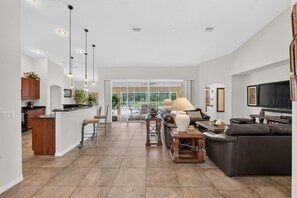 Een ruime woonkamer met een grote bank, een eettafel en een keuken met houten kastjes en een bar.