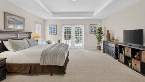 A bedroom with a bed, a TV, a dresser, and a door leading to a balcony. - Villa Corthouts: Luxury home close to bike trail! (Inverness)