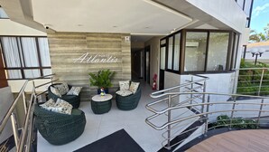 A modern outdoor seating area with wicker furniture and a stone wall backdrop. - Porto Atlantis Vista Mar 308 by La Playa (Ipojuca)