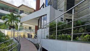 A modern building with a glass facade, a wooden walkway, and metal railings. - Porto Atlantis Vista Mar 308 by La Playa (Ipojuca)