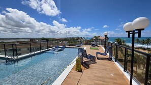A rooftop pool with clear blue water, surrounded by lounge chairs and a wooden deck. - Porto Atlantis Vista Mar 308 by La Playa (Ipojuca)