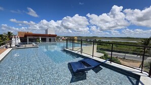 A rooftop pool with clear blue water, a lounge chair, and a view of the landscape. - Porto Atlantis Vista Mar 308 by La Playa (Ipojuca)