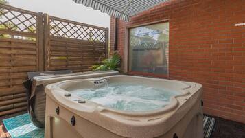 Un jacuzzi en un espacio exterior con paredes de ladrillo, cerca de una valla de madera y una puerta de cristal que muestra una dirección web.