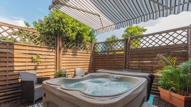 Een hottubgedeelte met een houten omheining, een overdekt terras en potplanten.