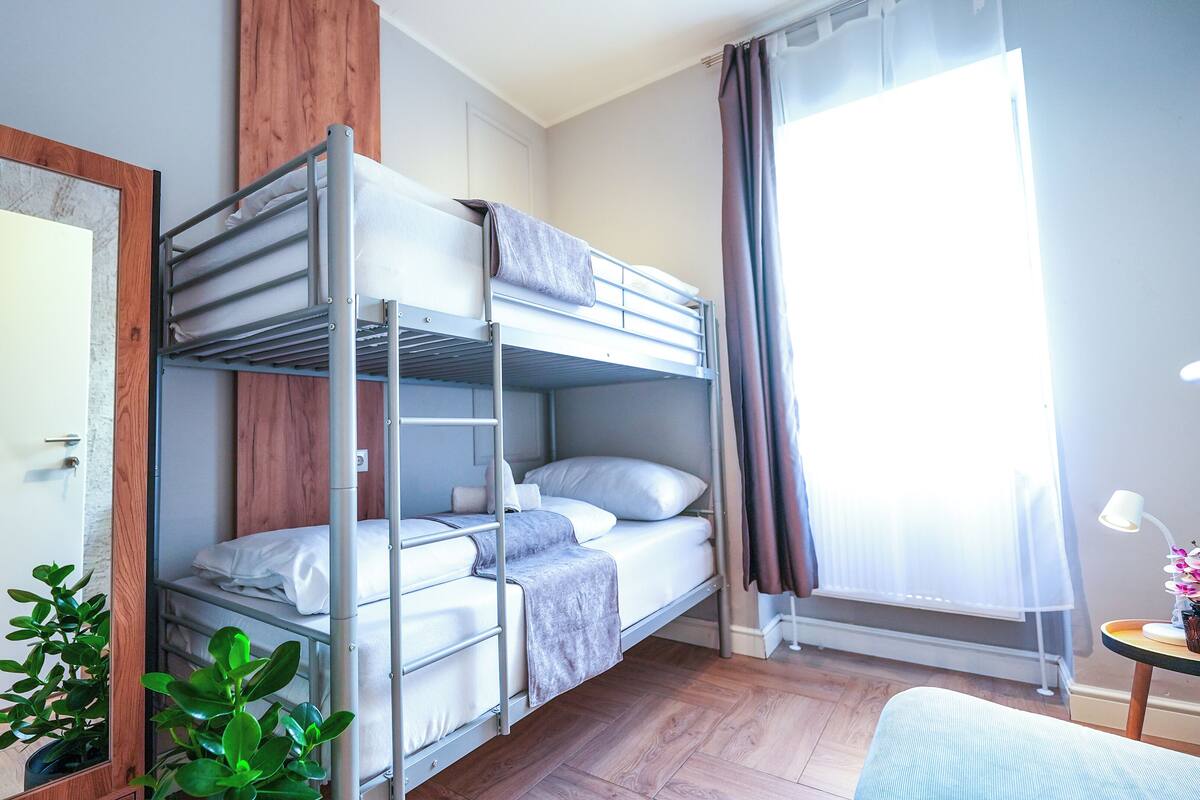 A bunk bed room with a wooden door, a small table with a lamp, and a potted plant.