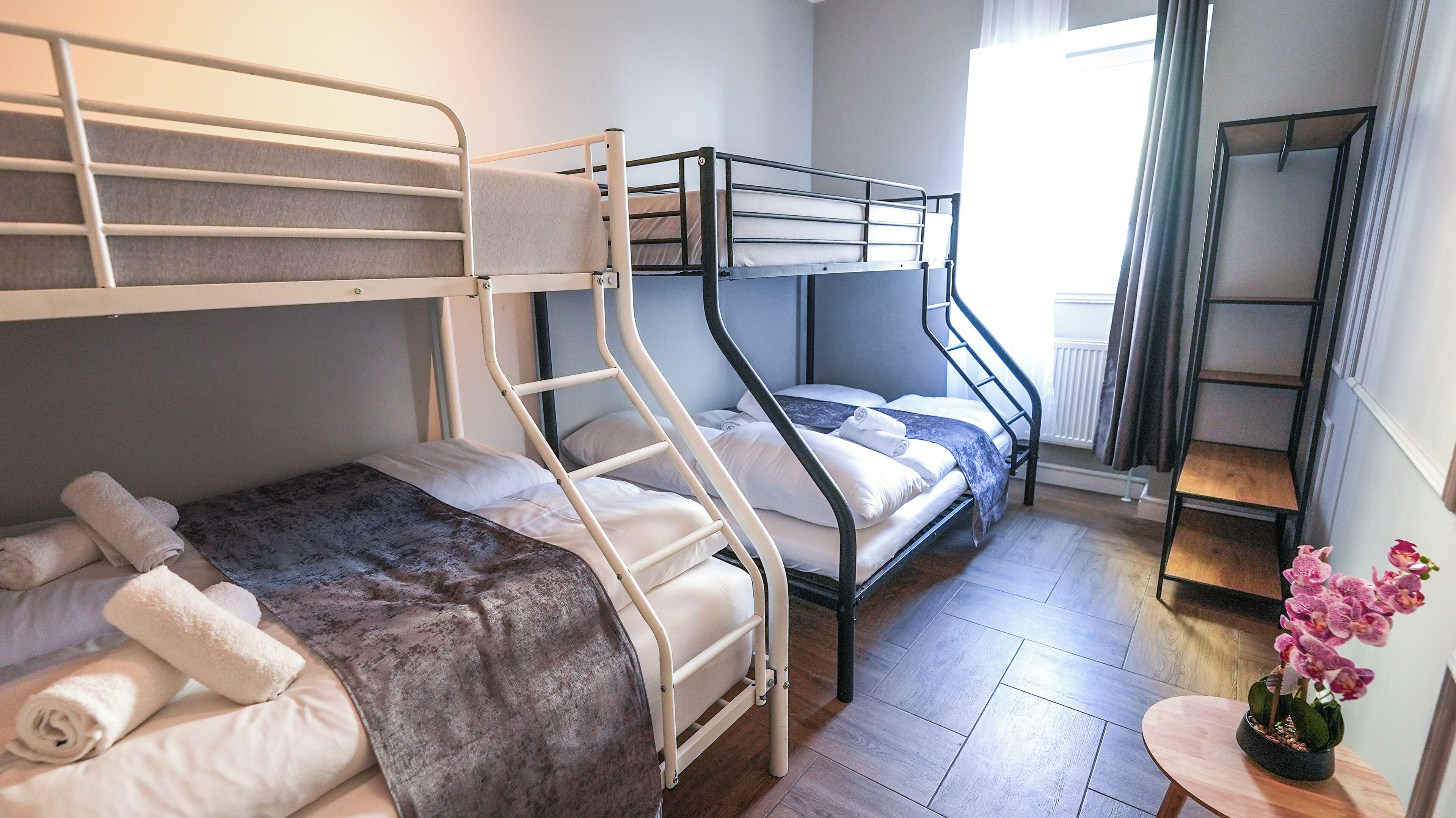 A bunk bed room with a ladder, a small table with a plant, and a window with curtains.