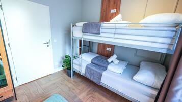Habitación con literas, suelo de madera, una planta en maceta y una puerta blanca.