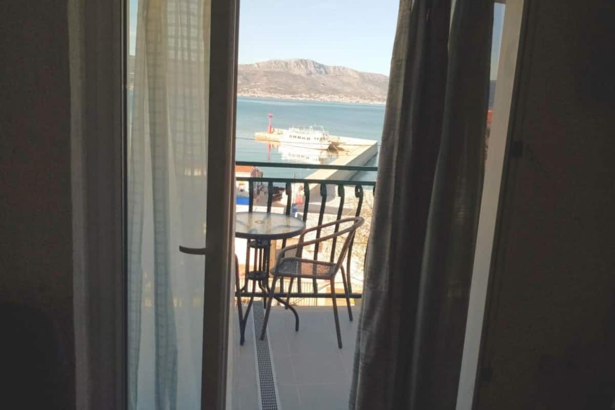A balcony with a table and chairs, overlooking a body of water and a distant mountain range.