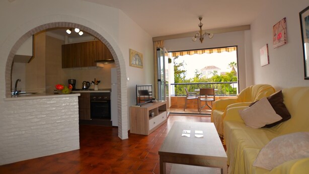 Una sala de estar con un sofá, una mesa de centro y una zona de cocina con armarios y estufa.