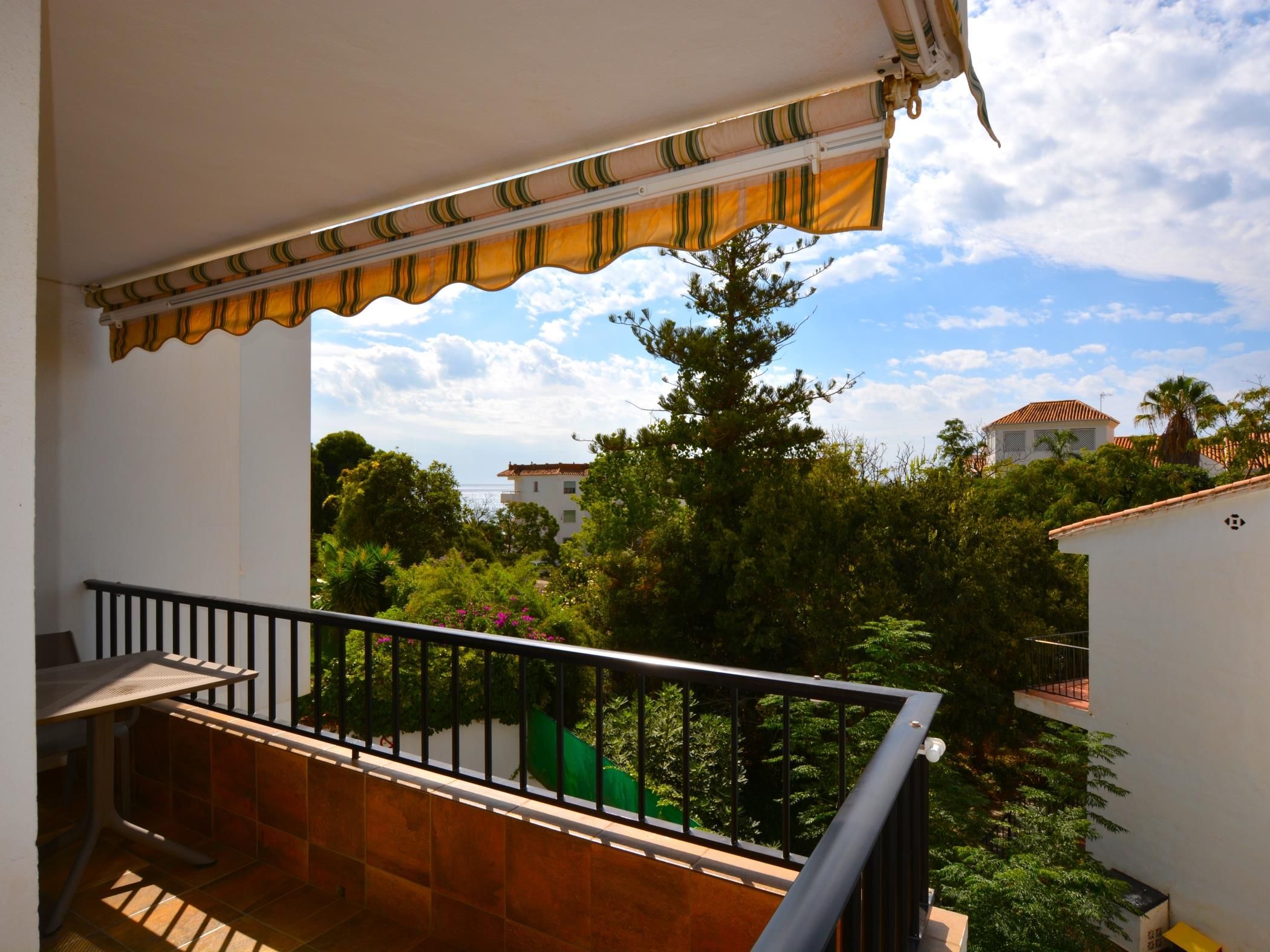 Un balcón con vistas a una zona residencial, barandilla y suelo de baldosas.