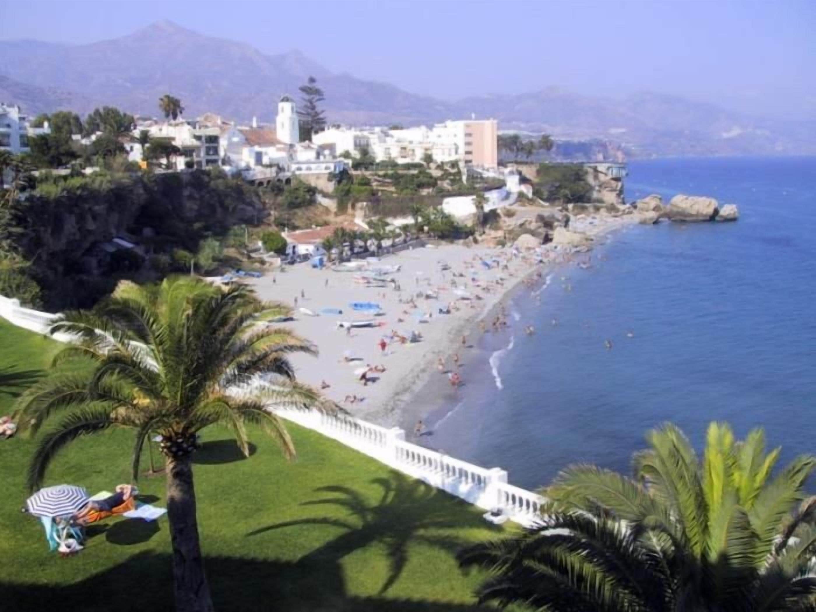 A coastal town with a beach, buildings, and a mountain in the background.