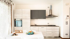 A modern kitchen with light wood cabinets, a stainless steel range hood, and a white dining table with chairs.