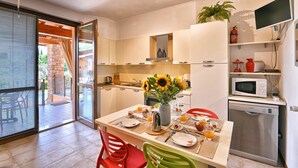 Una cocina moderna con armarios blancos, un microondas integrado y un lavavajillas. Hay una mesa de comedor puesta con platos, cubiertos y un jarrón con girasoles.