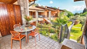 Una terraza con una mesa y sillas, un muro de piedra, y vistas a una casa con jardín y montañas al fondo.