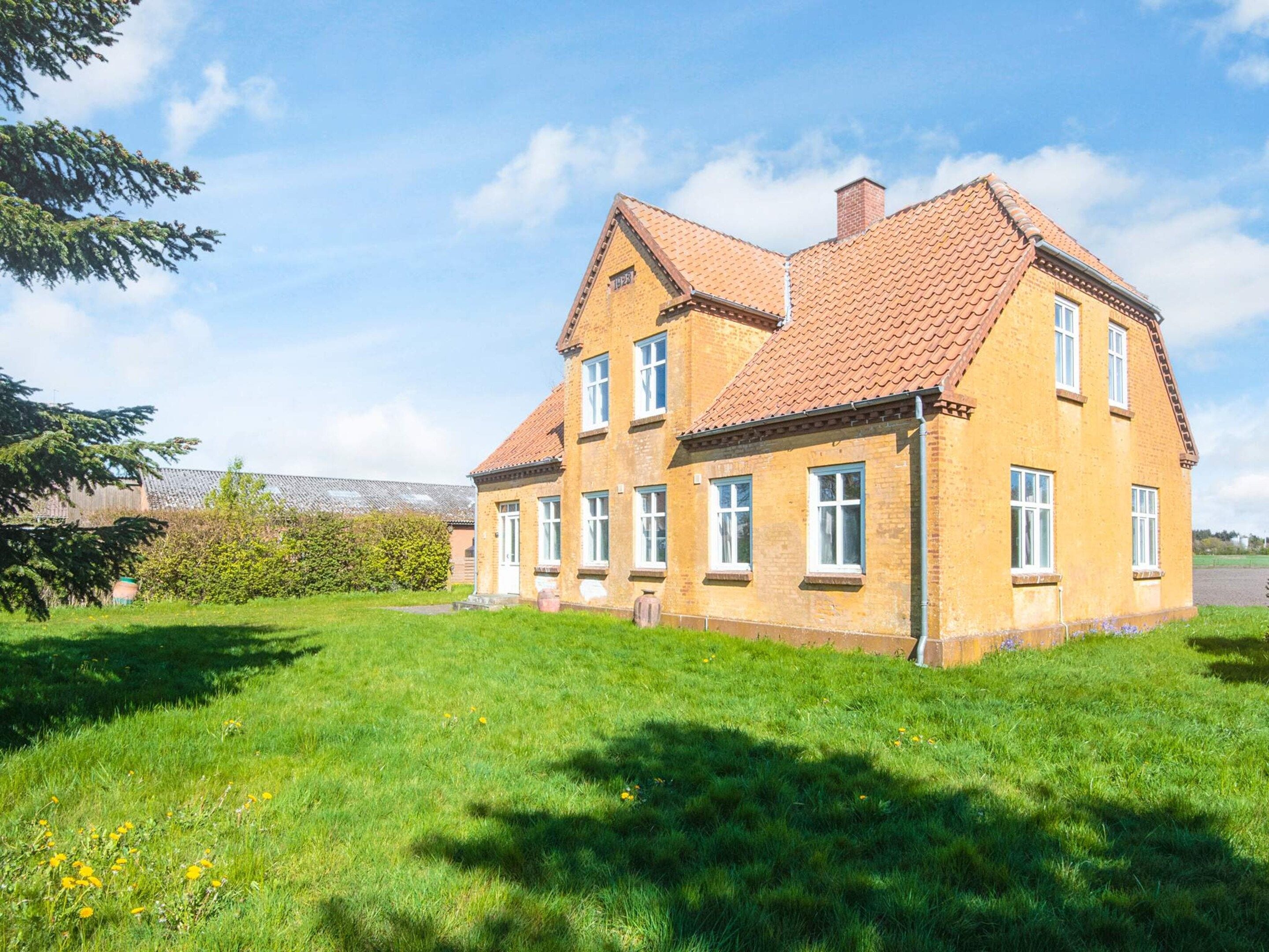 A two-story house with a red-tiled roof, surrounded by a grassy lawn and a tree.