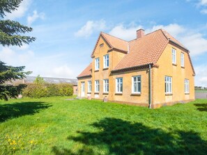A two-story house with a red-tiled roof, surrounded by a grassy lawn and a tree. - 4 Person Holiday Home in Skaerbaek (Skaerbaek)