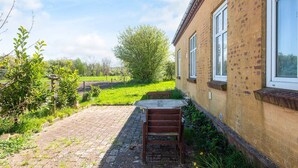 A brick building with a paved patio and a wooden bench. - 4 Person Holiday Home in Skaerbaek (Skaerbaek)