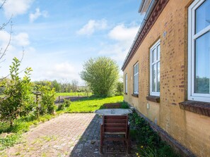 A brick building with a paved patio and a wooden bench. - 4 Person Holiday Home in Skaerbaek (Skaerbaek)