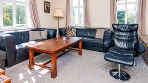 A living room with a wooden coffee table, a black leather sofa, a black leather armchair, and a lamp. - 4 Person Holiday Home in Skaerbaek (Skaerbaek)