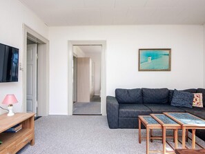 A living room with a grey sofa, a wooden coffee table, a TV on the wall, and a painting. - 4 Person Holiday Home in Skaerbaek (Skaerbaek)